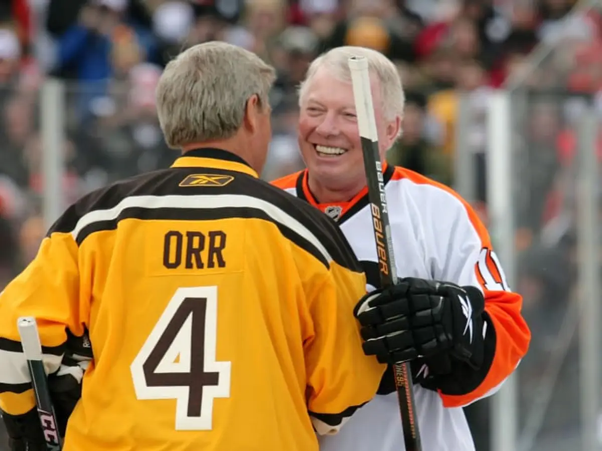 Bobby Orr raising the Stanley Cup in a Boston Bruins jersey, showing his skates and uniform details